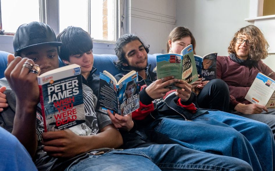 Photo of five teenagers sat on a sofa reading various copies of Quick Reads books