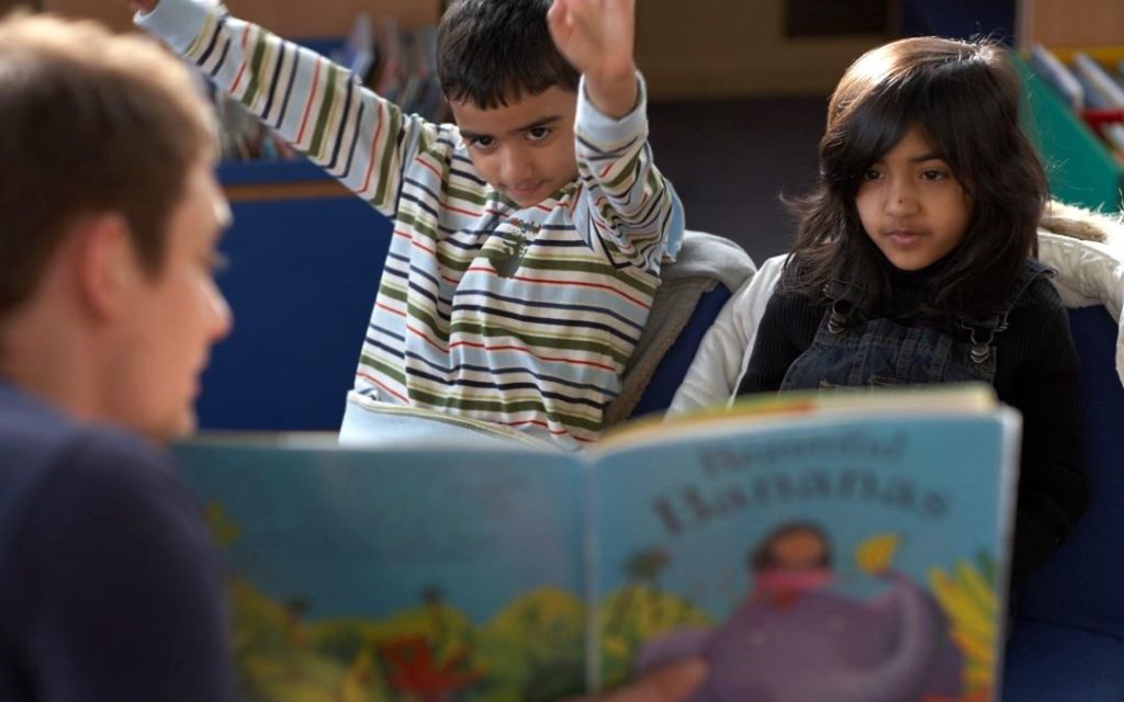 Photo of an adult man reading a book to two children. 