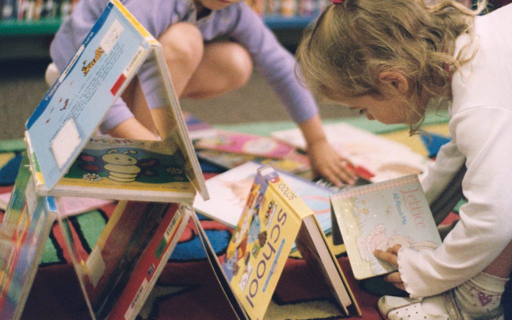 A photo of two young children making a tower out of books.
