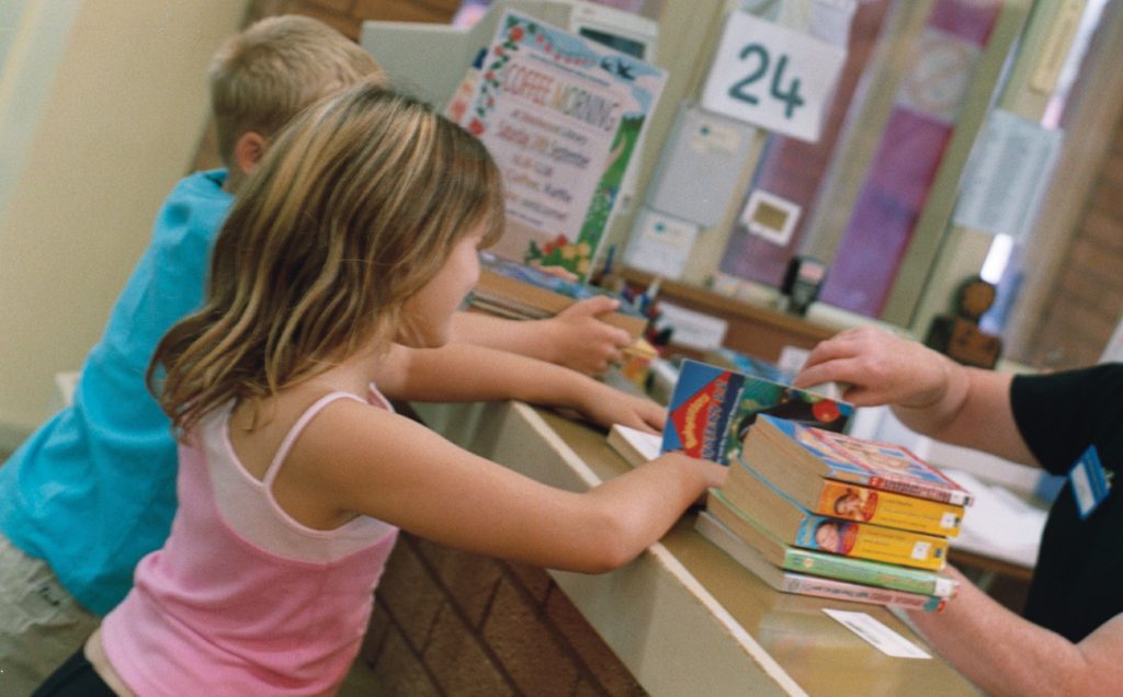 A photo of two children taking out some books from the library.