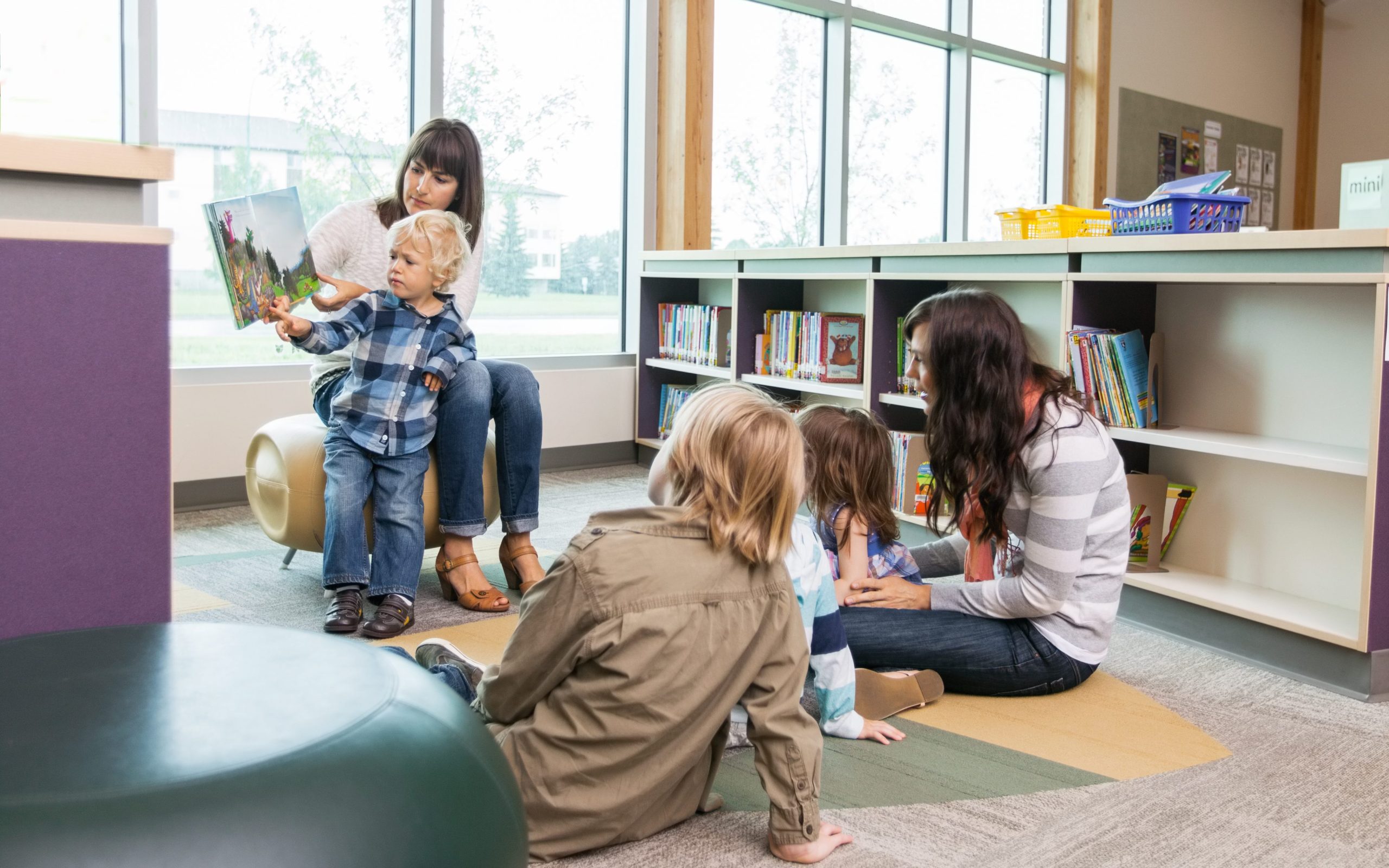 Photo of young children and adults sat on a library floor looking at books.