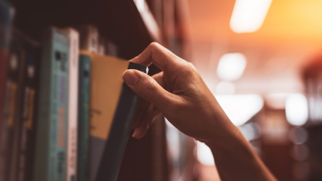Photo of a hand pulling a book from a book shelf.